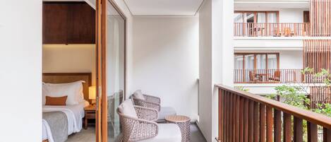 Un balcón con mobiliario de mimbre, una cama con ropa de cama blanca y vistas del exterior del edificio.