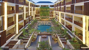 A multi-story hotel with a central courtyard featuring a swimming pool, outdoor seating, and potted plants. - The Magani Hotel and Spa (Legian)