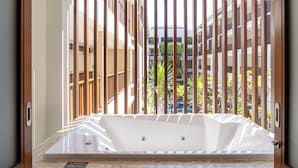 A bathroom with a bathtub, wooden slats, and a view of a building with balconies and greenery. - The Magani Hotel and Spa (Legian)
