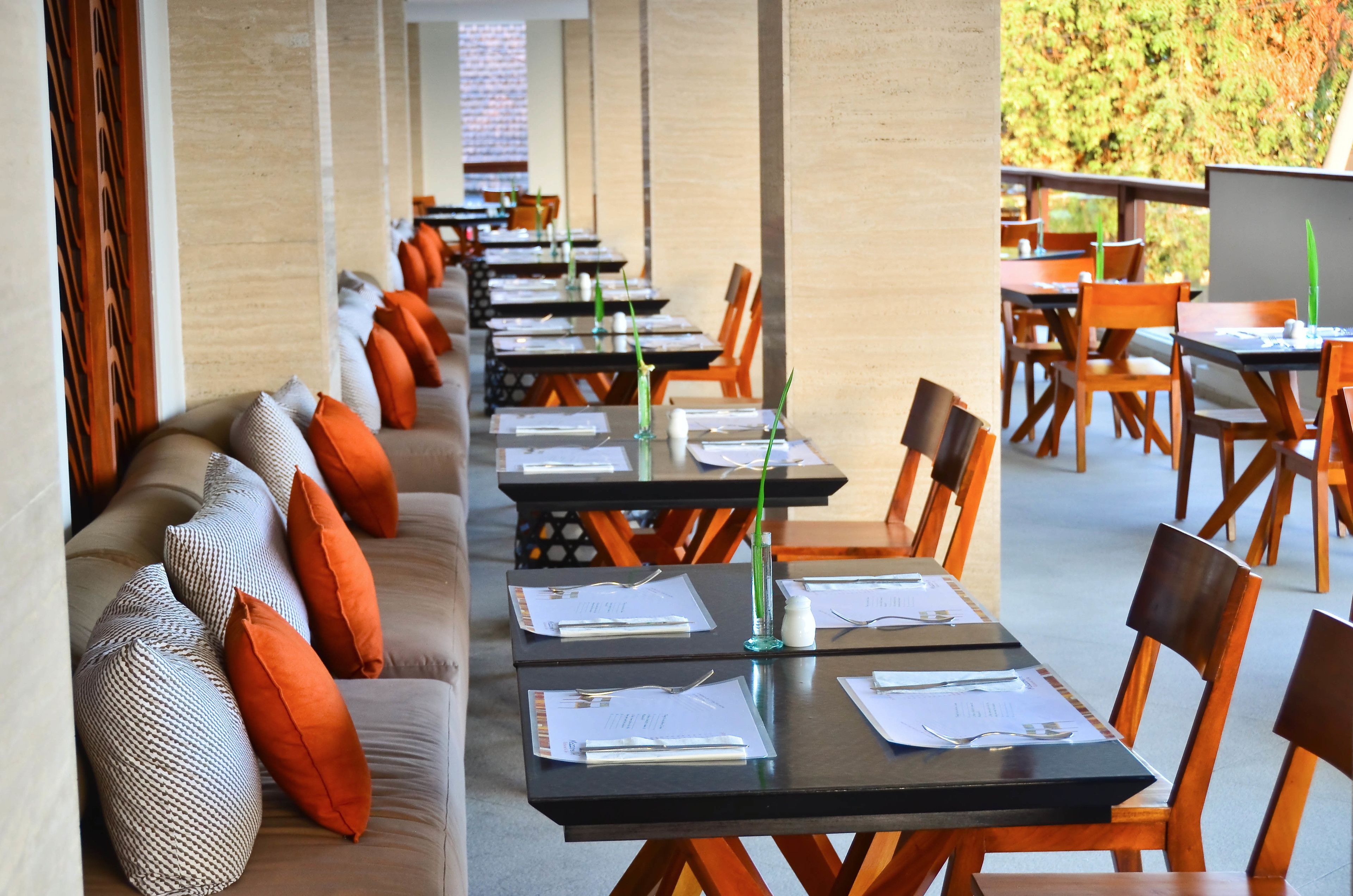 Una larga mesa de comedor con sillas, un sofá con cojines anaranjados y un jarrón de cristal con una planta verde.