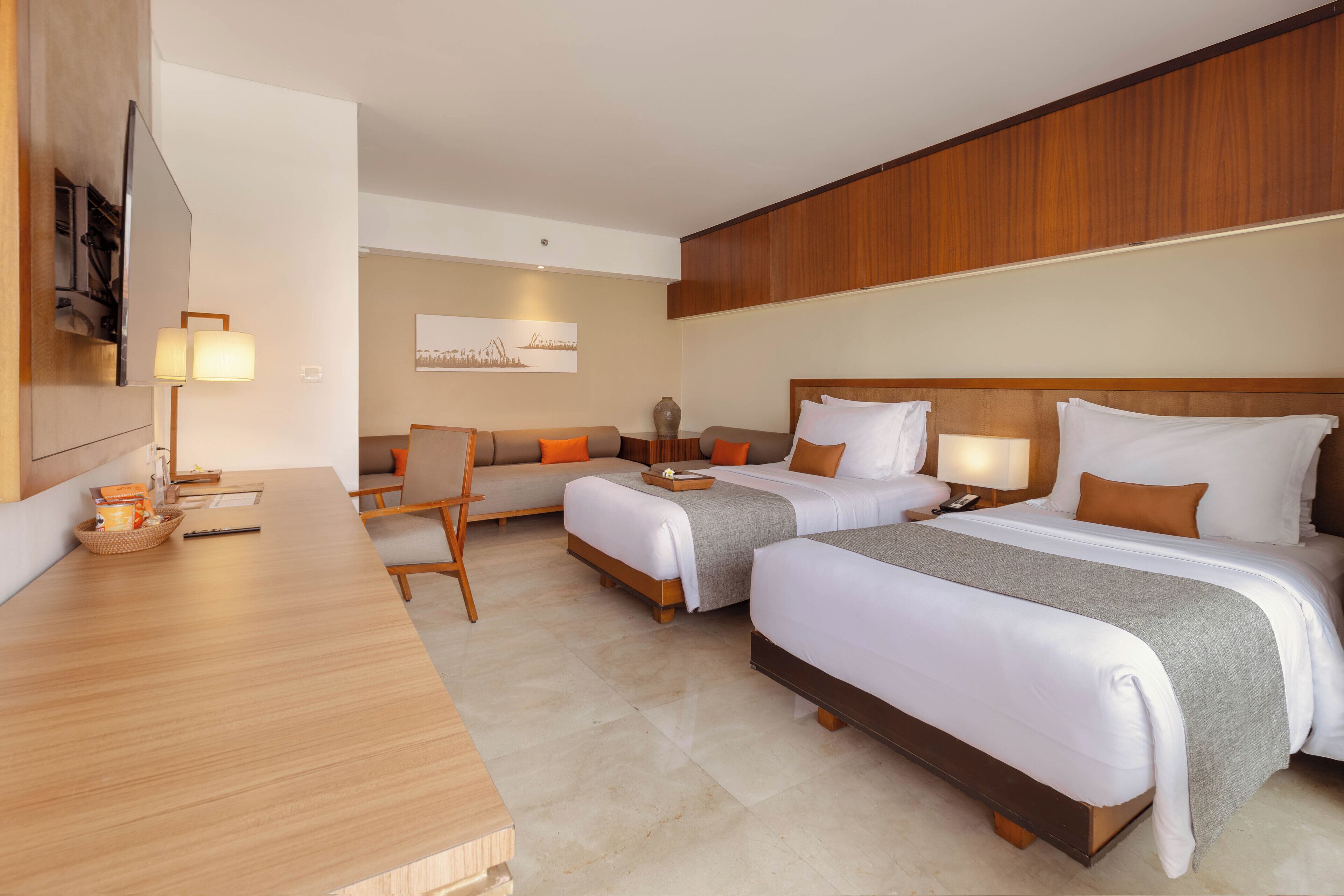 A hotel room with two beds, a desk, a chair, a TV, and a wall-mounted lamp.