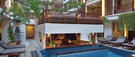 A hotel with a pool area, lounge chairs, and a two-story balcony with wooden railings.