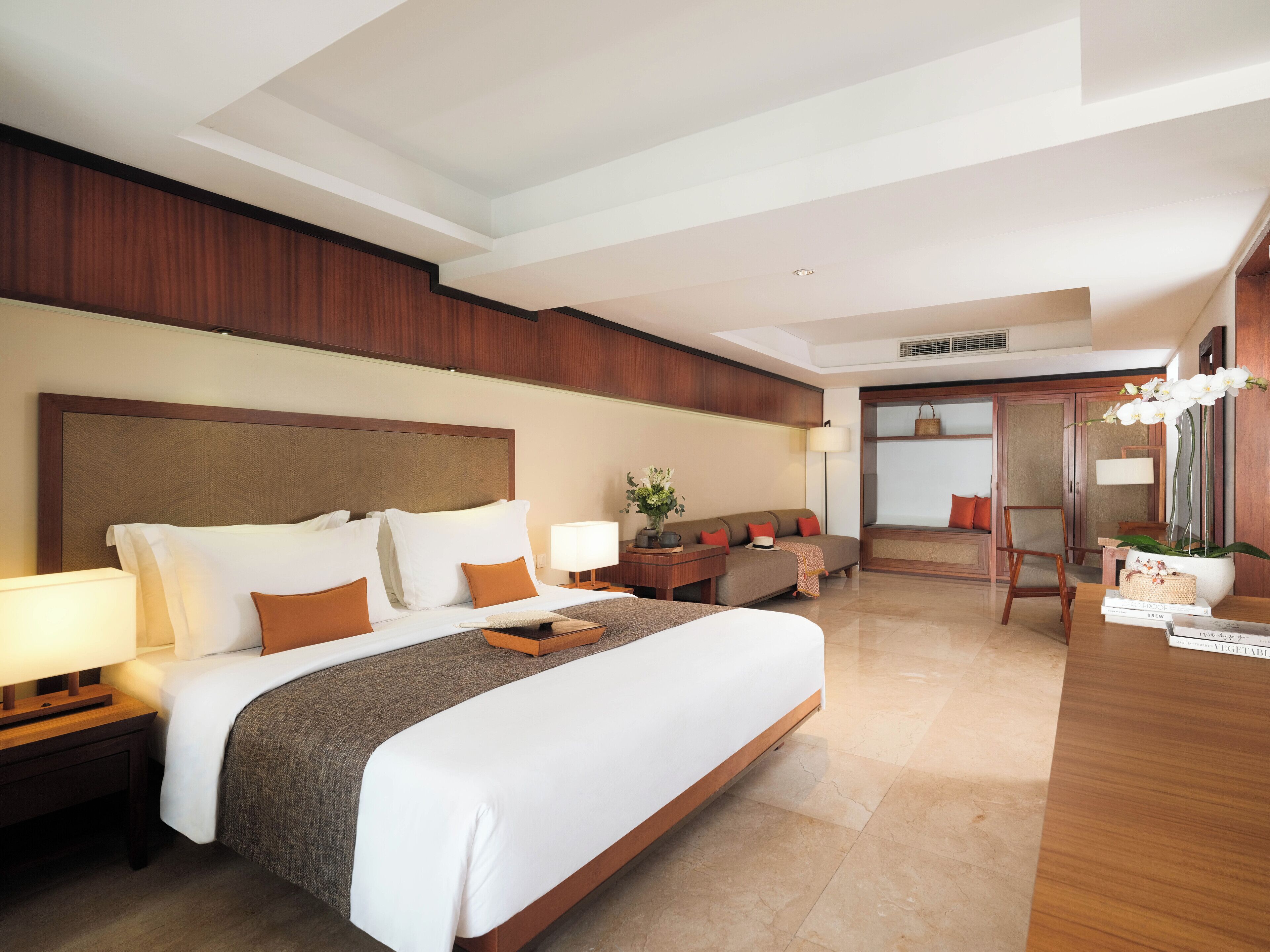 A hotel room with a large bed, bedside tables, a sofa, a desk, and a mirror.