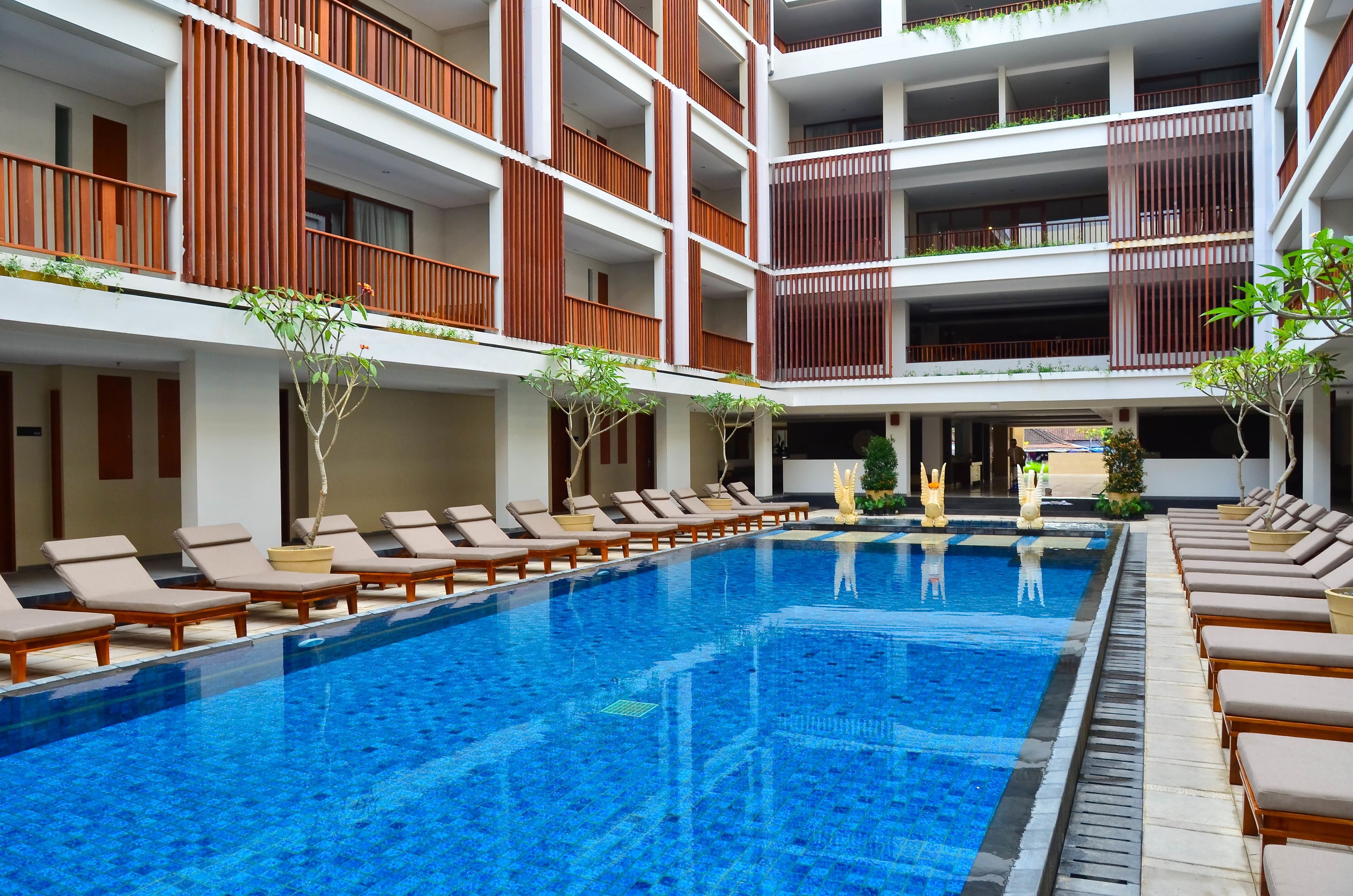 Un hotel de varios niveles con una piscina central rodeada de sillones de descanso.