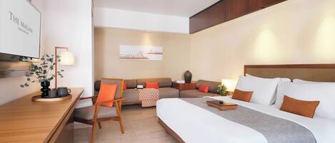 A hotel room with a bed, a sofa, a chair, a desk, and a TV.