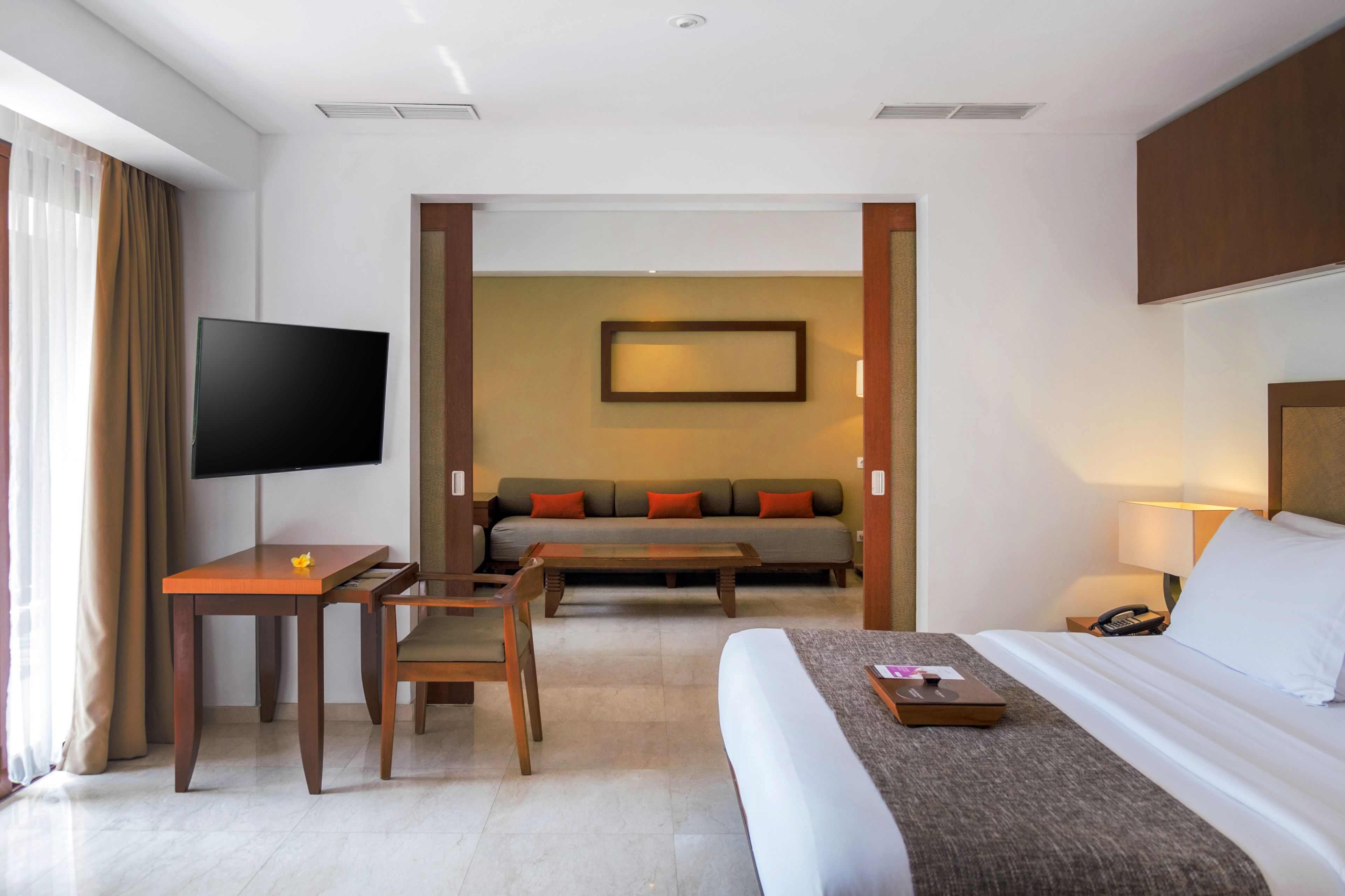 A hotel room with a bed, a desk with a chair, a sofa, a television, and a framed picture on the wall.