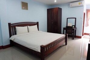 A bedroom with a wooden bed, a wardrobe, a desk with a mirror, and an air conditioner on the wall.