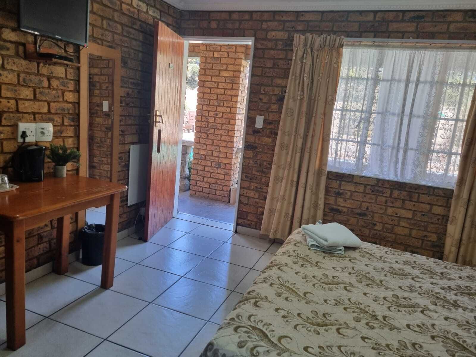 A hotel room with a bed, a wooden table, a TV, and a brick wall.