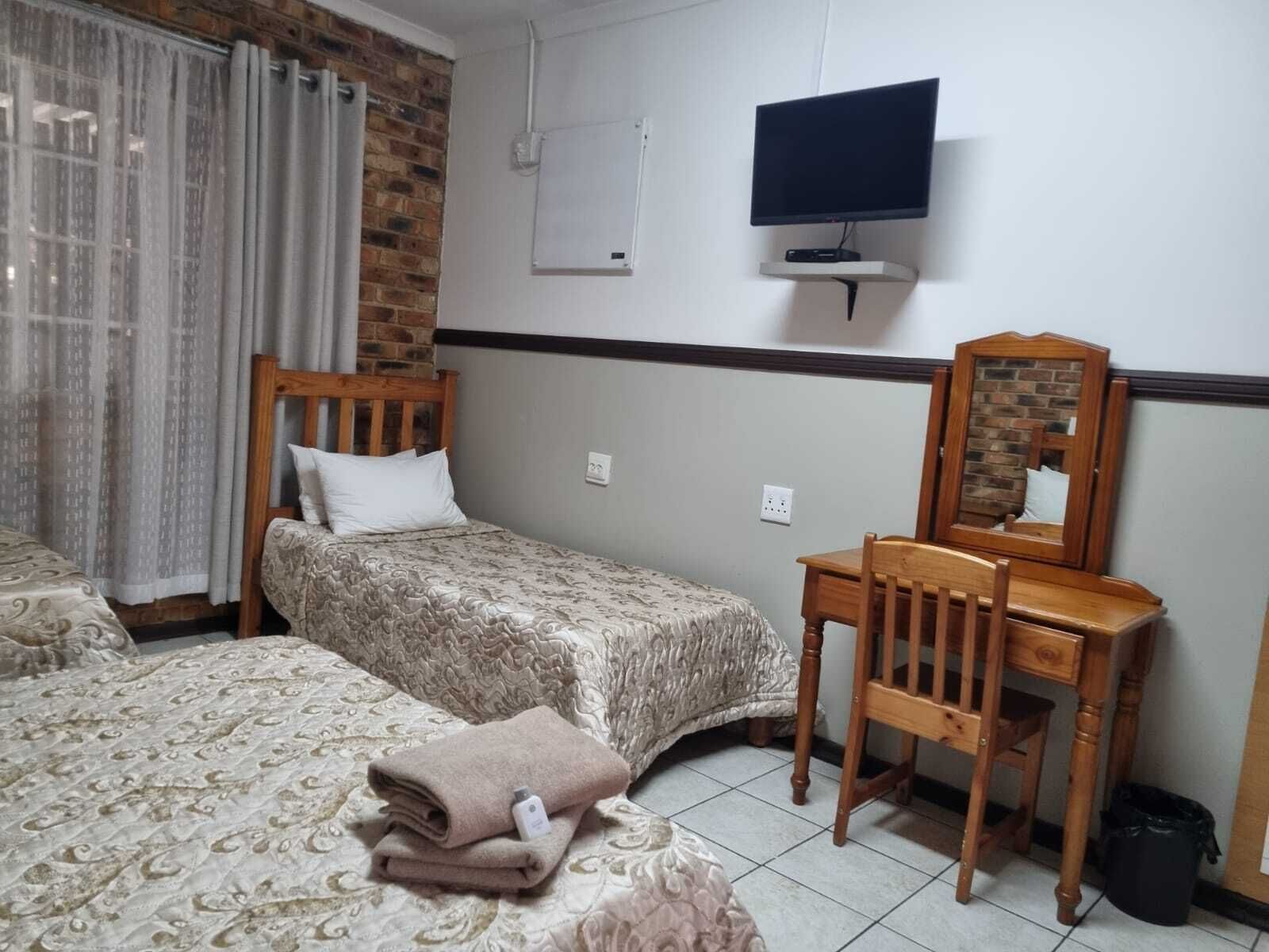 A bedroom with a bed, a desk with a chair, a television, and a mirror.