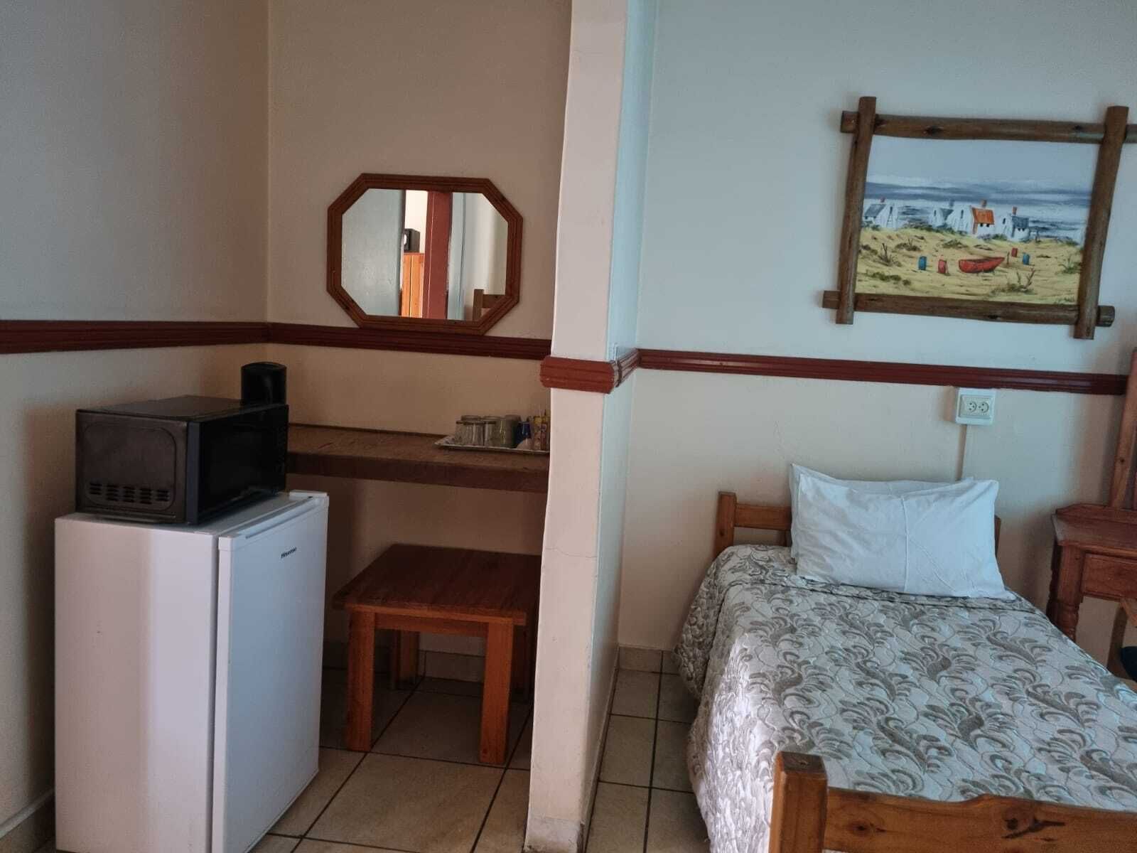 Una stanza compatta con un letto, una piccola scrivania con un forno a microonde, una sedia e uno specchio.