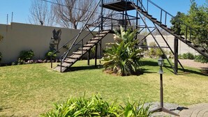 A metal staircase structure in a garden with a mural on the wall.