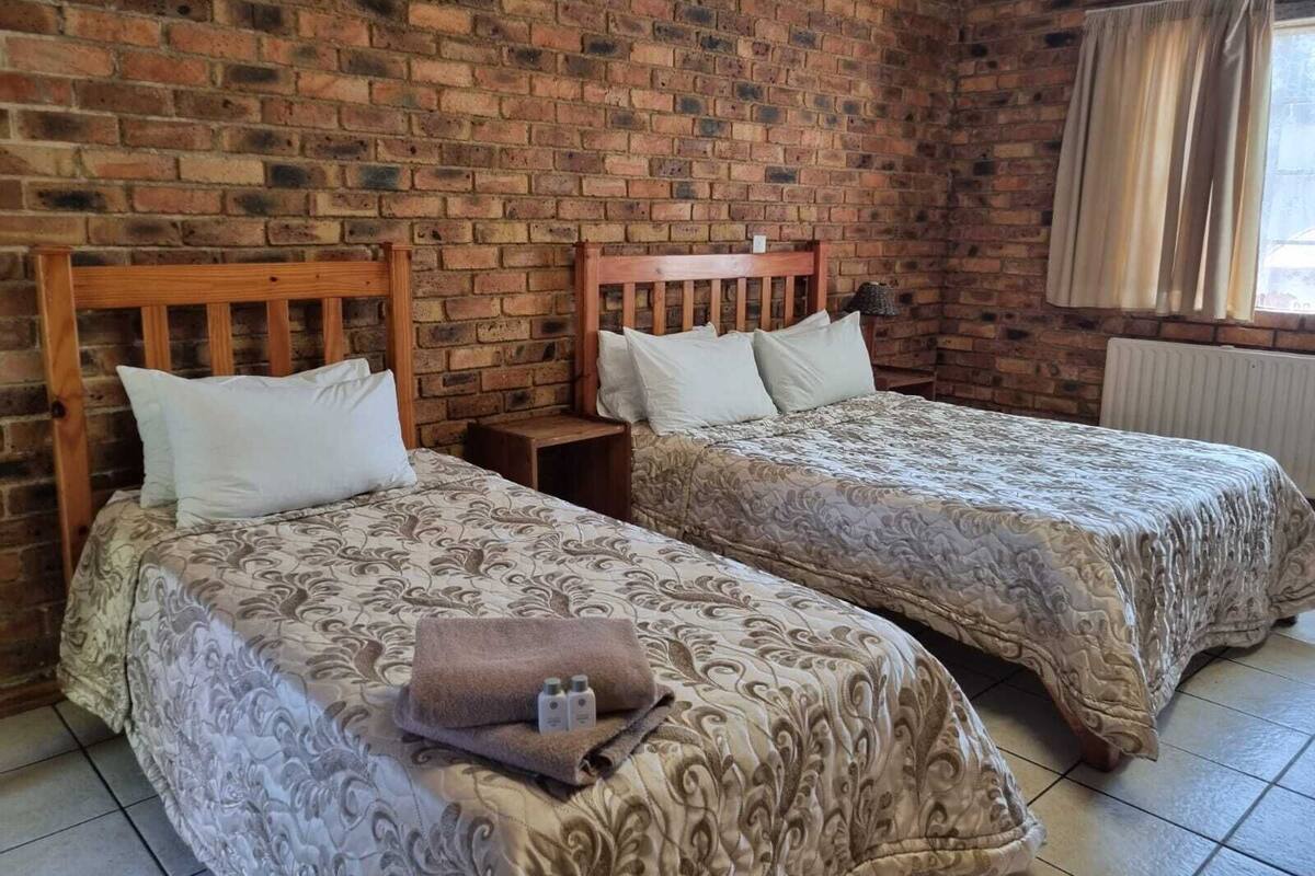 Une chambre avec deux lits, un mur en briques, une fenêtre avec des rideaux et un sol carrelé.