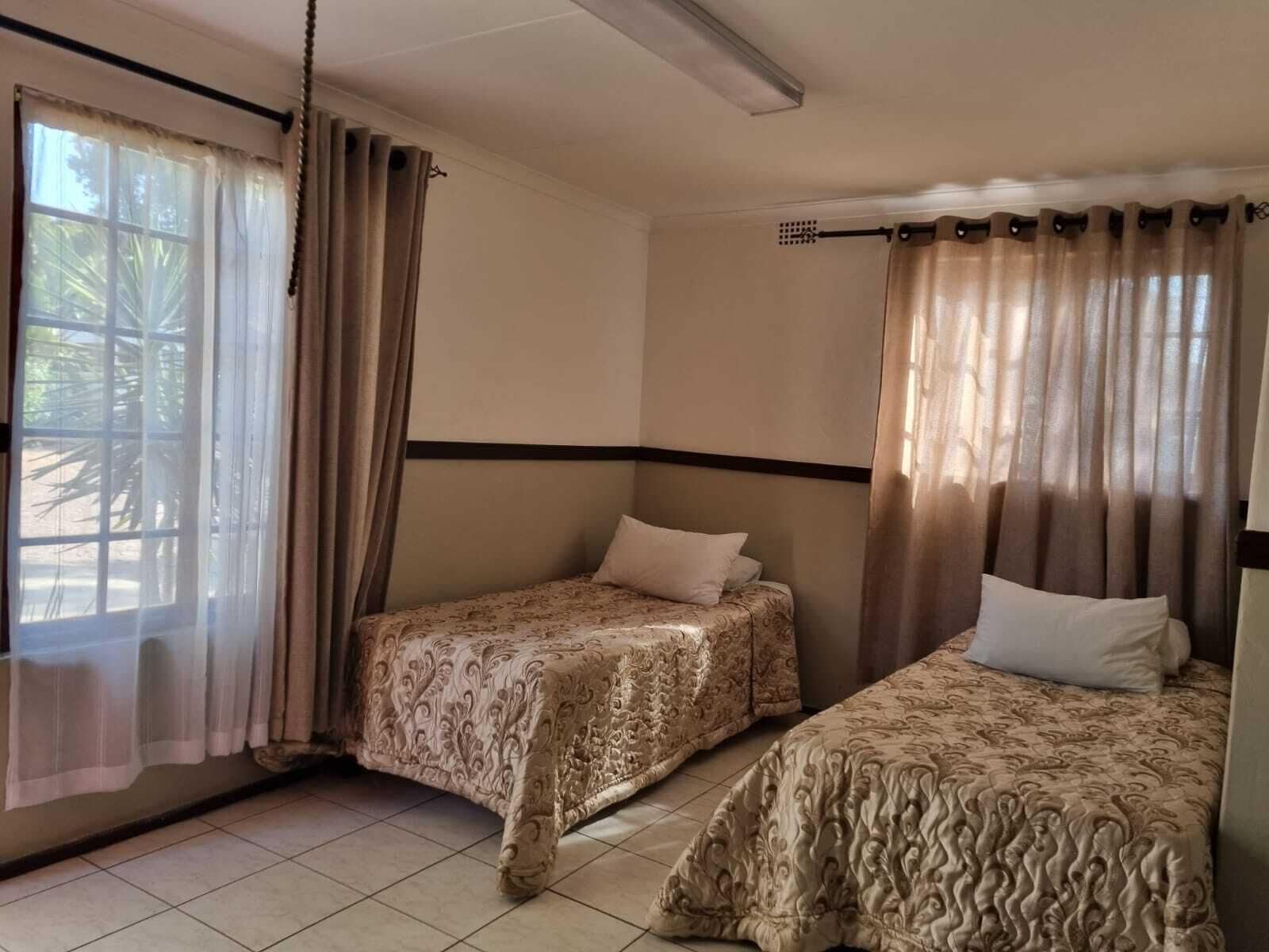 Una habitación con dos camas, cortinas color beige y piso de baldosas.