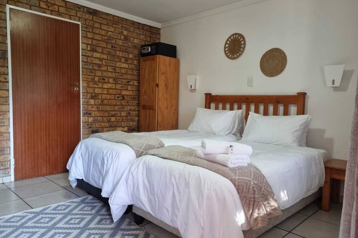 Une chambre avec un mur en briques, une tête de lit en bois, un lit avec une literie blanche, une table de chevet et un tapis à motifs.