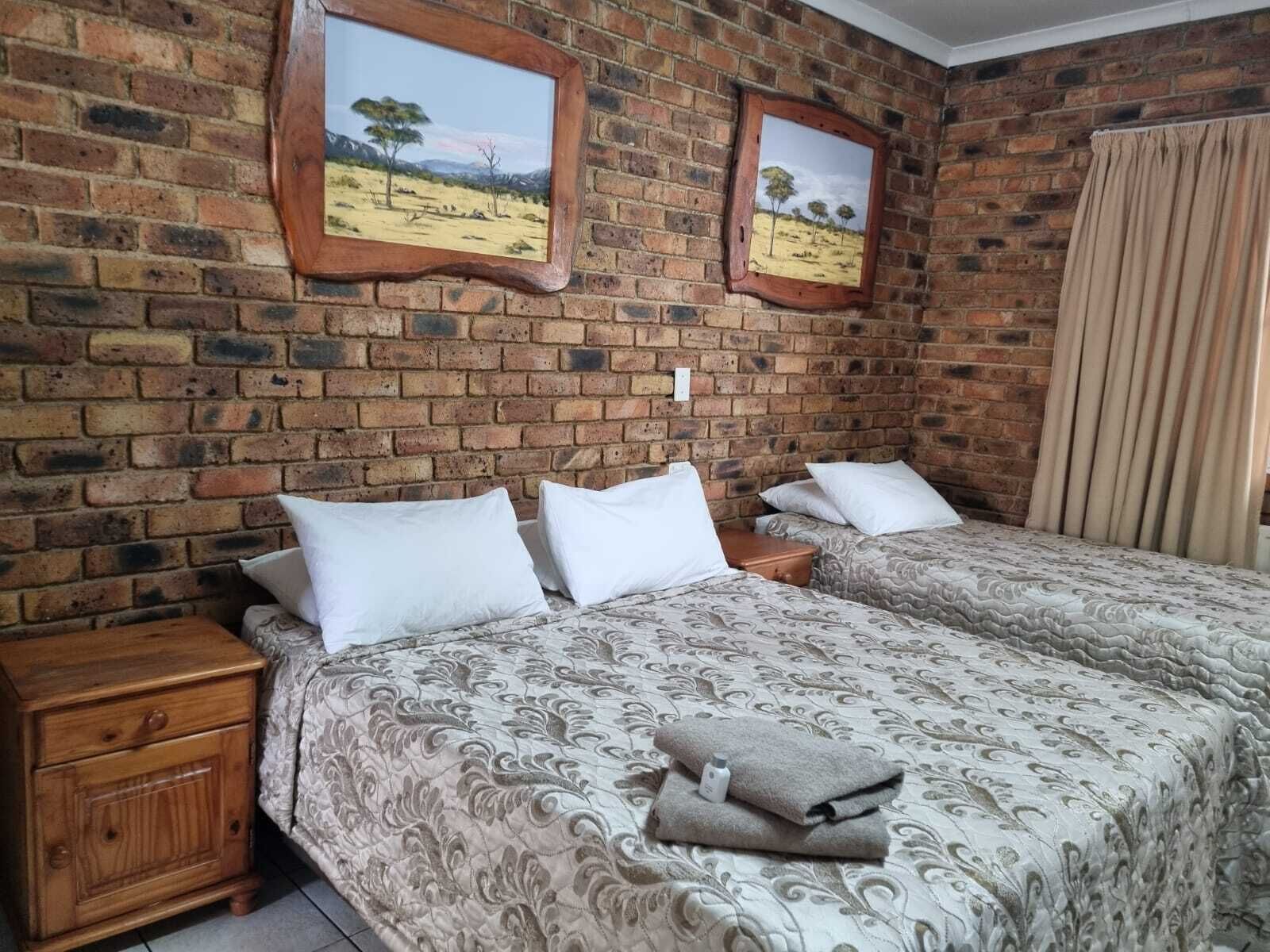 Ein Zimmer mit zwei Betten, Holz-Nachttischen und einer Ziegelwand mit zwei gerahmten Bildern.