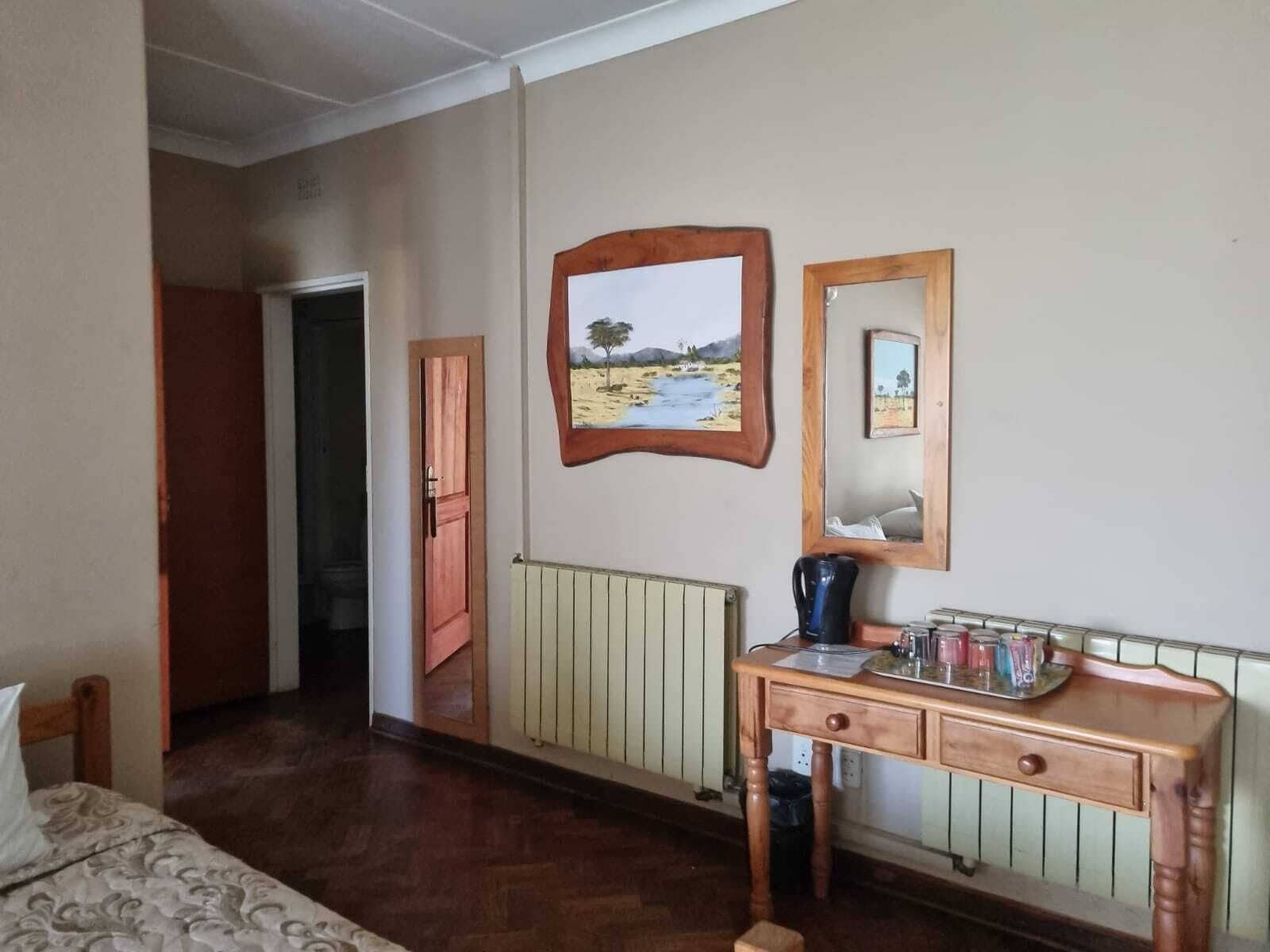 Una habitación con una cama, un escritorio de madera con un hervidor, un radiador y dos cuadros en la pared.