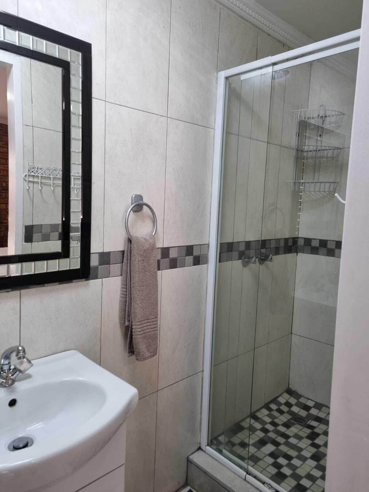 Un baño con lavamanos, espejo, toallero y cabina de ducha de vidrio.