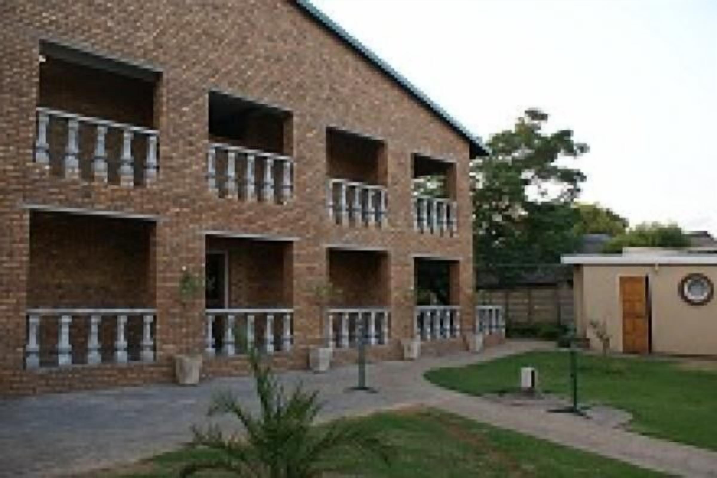 A multi-story brick building with balconies, a small garden area, and a separate building with a circular window.