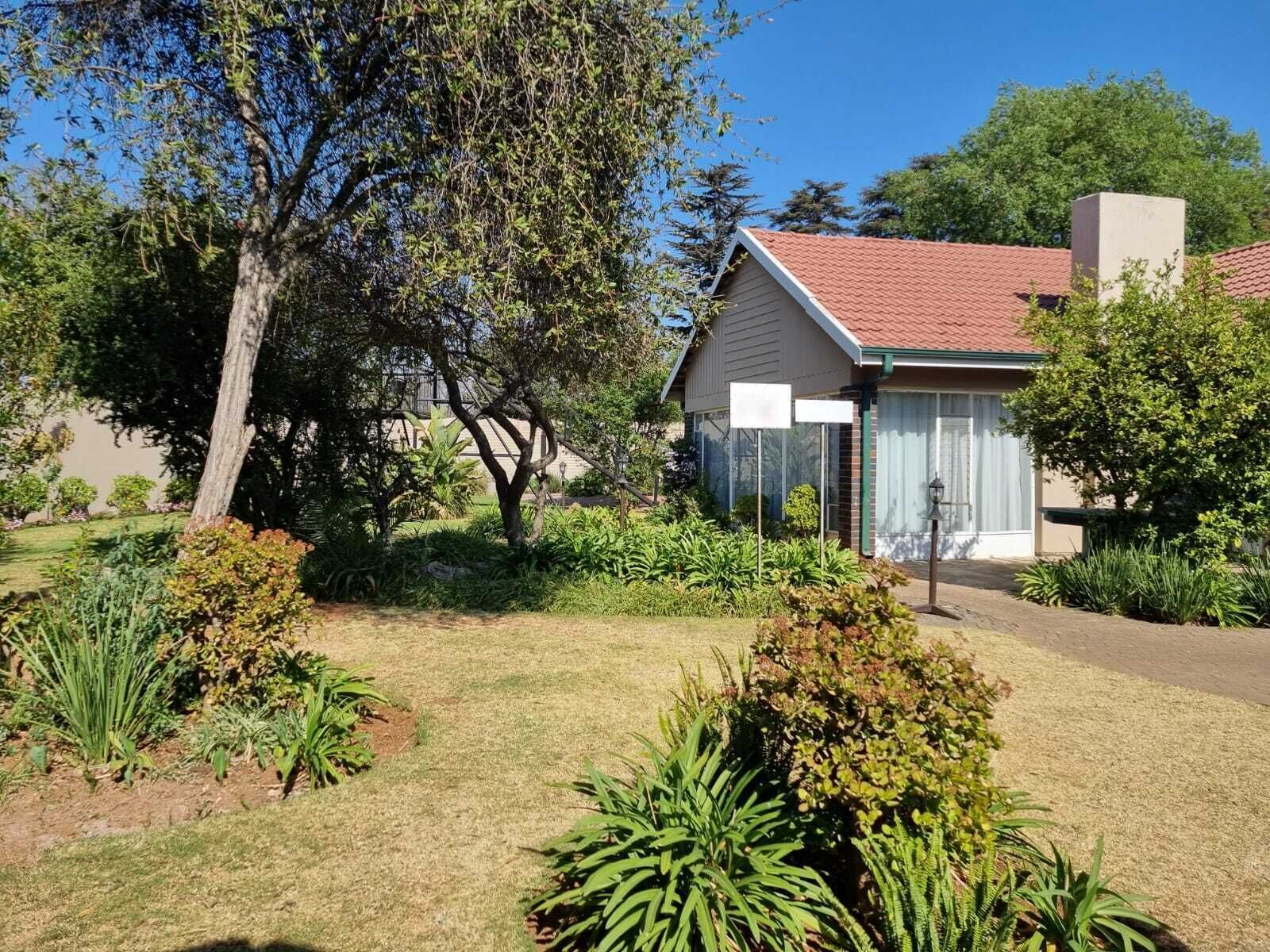 Ein Wohnhaus mit rotem Ziegeldach, umgeben von einem gepflegten Garten mit verschiedenen Pflanzen und einem großen Baum.