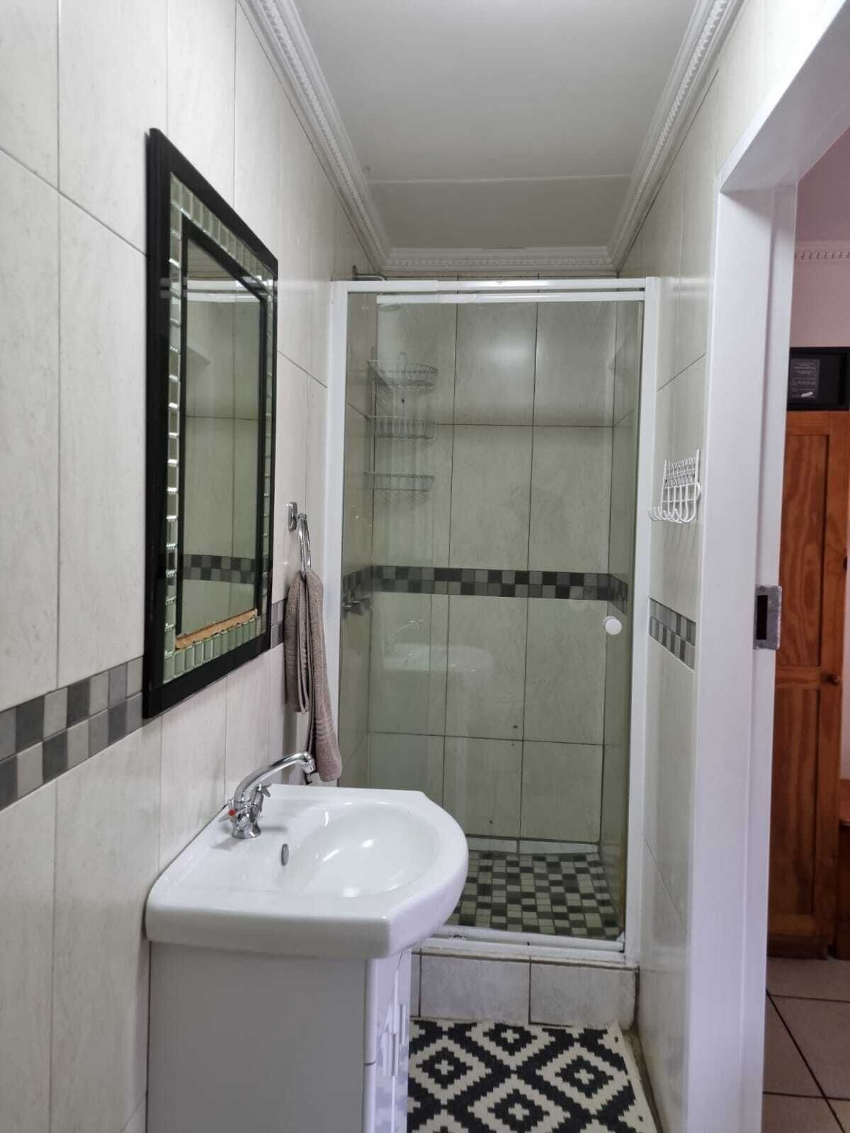 A bathroom with a white sink, a glass-enclosed shower, and a mirror with a black frame.