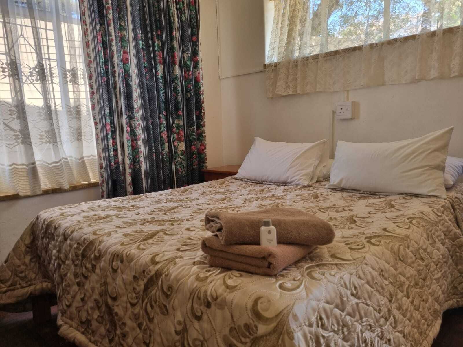 Ein ordentlich gemachtes Bett mit einem gemusterten Überwurf, ein Stapel gefalteter Handtücher und ein Nachttisch mit einer Lampe.