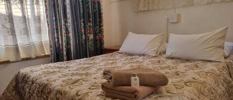 Una cama bien hecha con una colcha estampada, una pila de toallas dobladas y una mesita de noche con una lámpara.