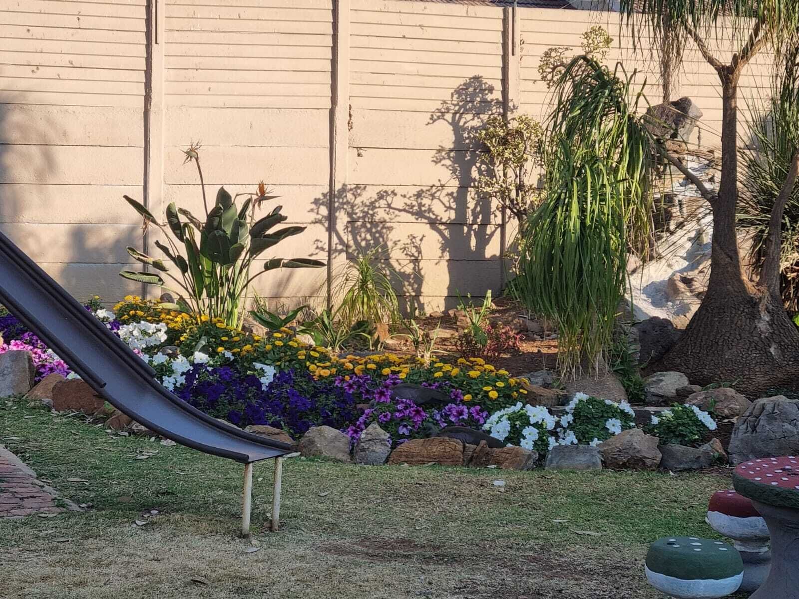 A garden with a variety of plants and flowers, a slide, and a rock garden.