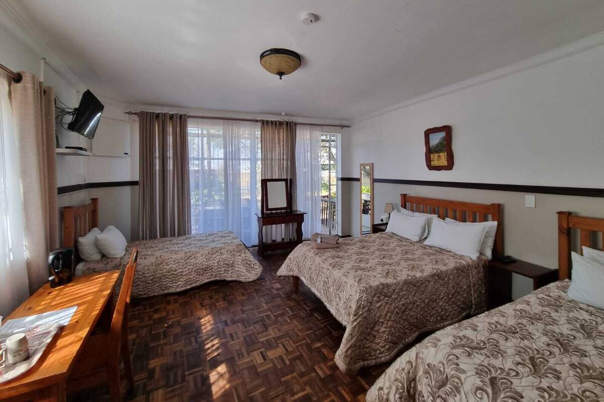 Une chambre d’hôtel avec deux lits, un bureau en bois, une télévision et une fenêtre avec des rideaux.
