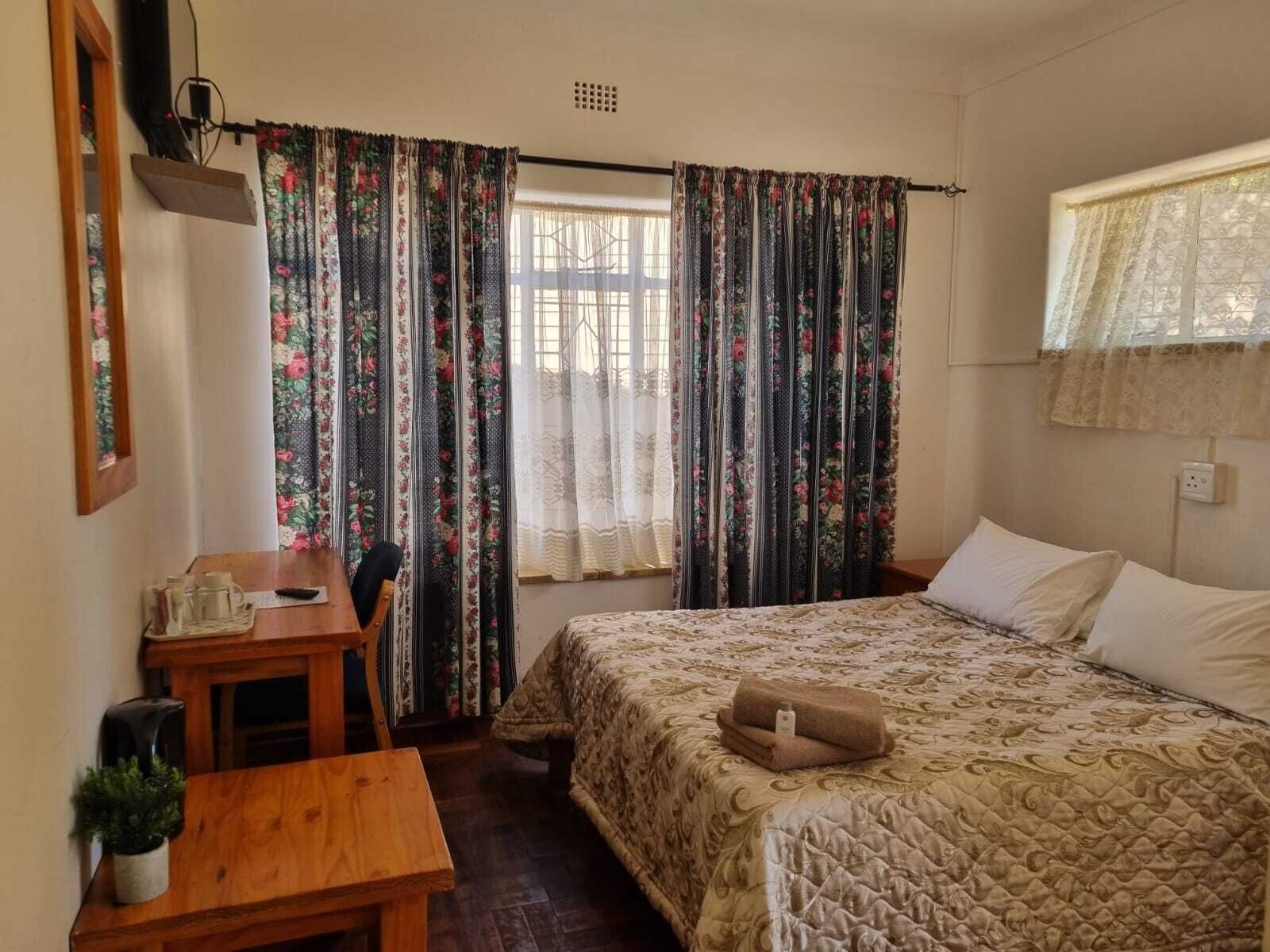 Un dormitorio con cama, escritorio y silla. Hay cortinas en las ventanas.