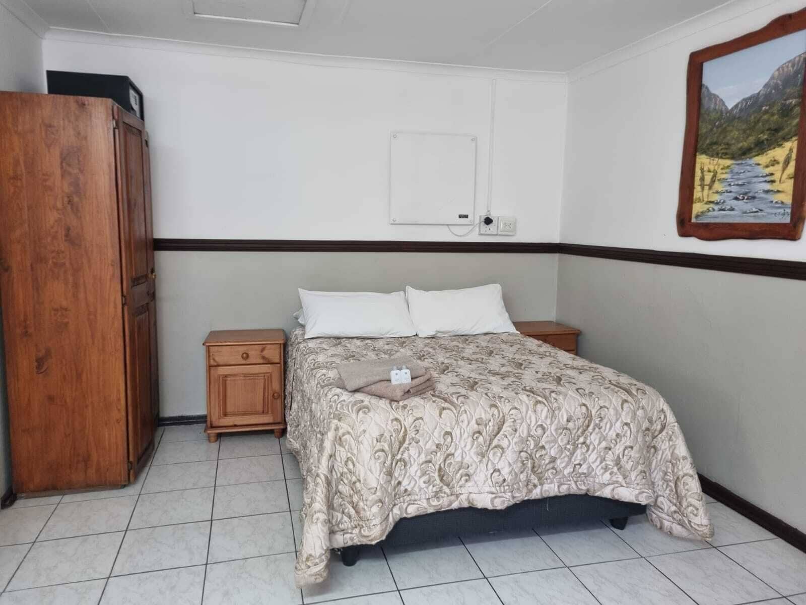 A bedroom with a bed, two bedside tables, a wardrobe, a wall-mounted electrical outlet, and a framed picture.