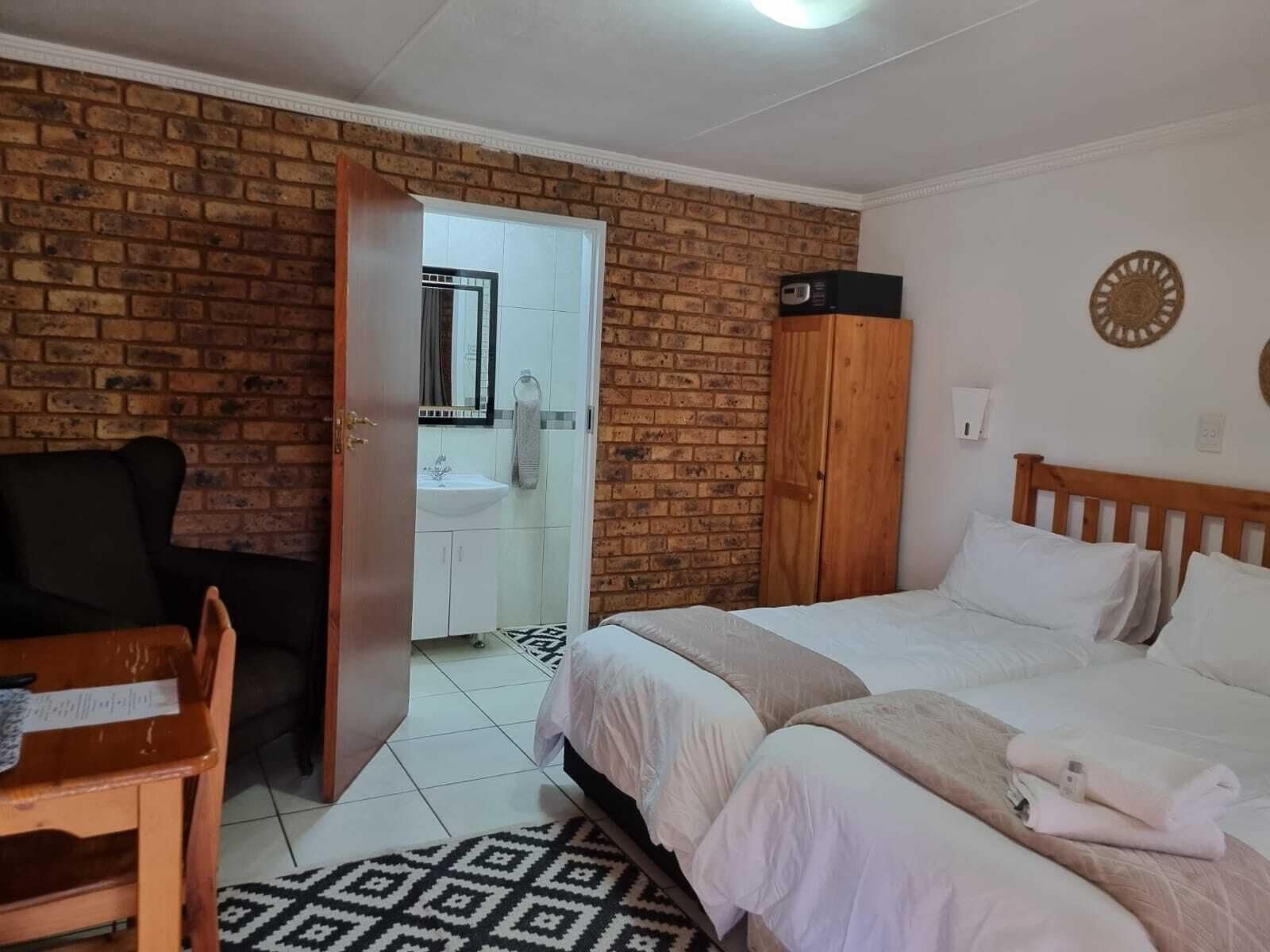 A hotel room with a brick wall, a wooden bed, a desk, and a bathroom visible through an open door.