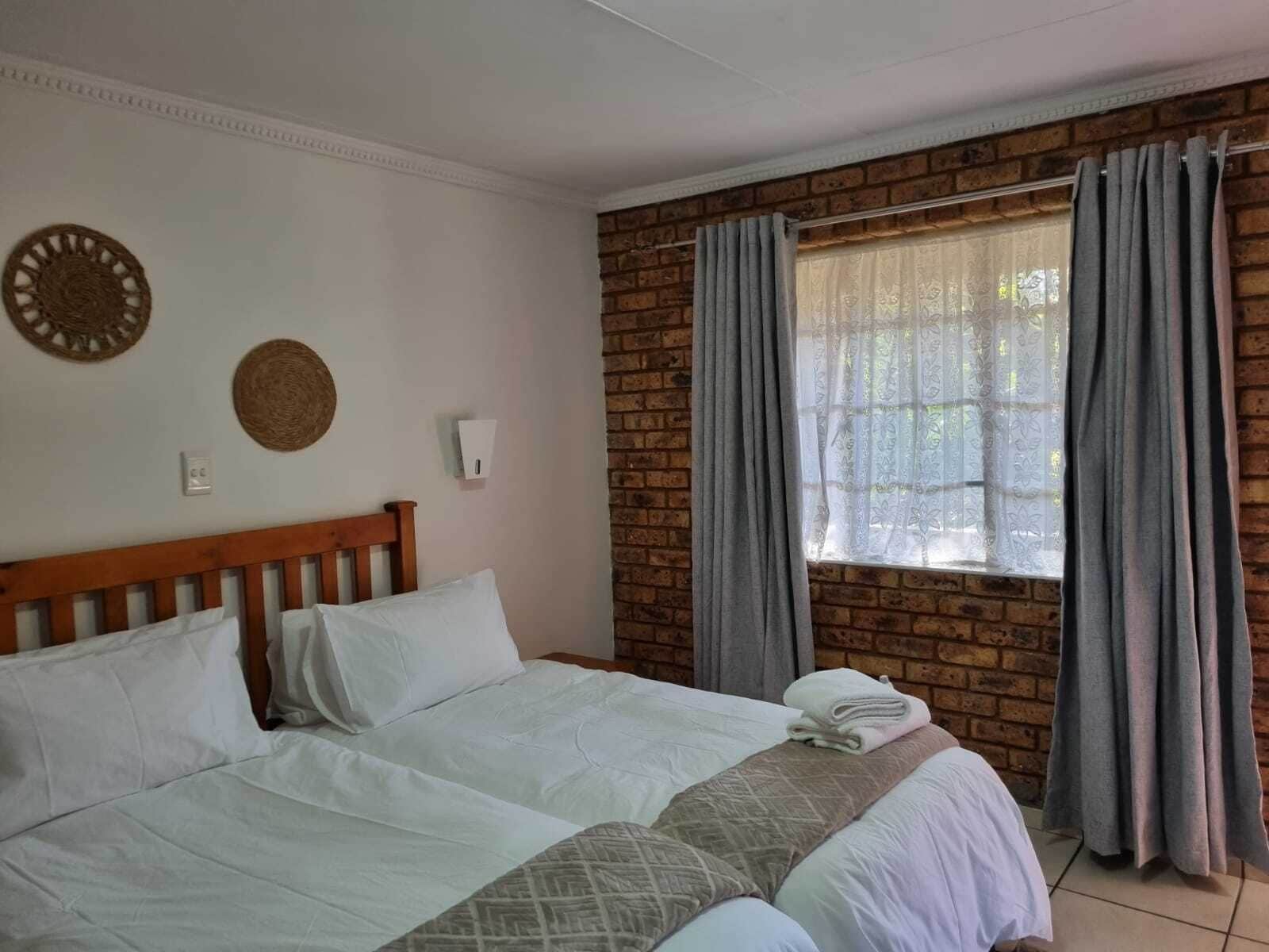A double bed with white linens, a wooden headboard, and a window with grey curtains.