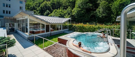 A hotel with a swimming pool, a covered outdoor area, and a mountainous backdrop.