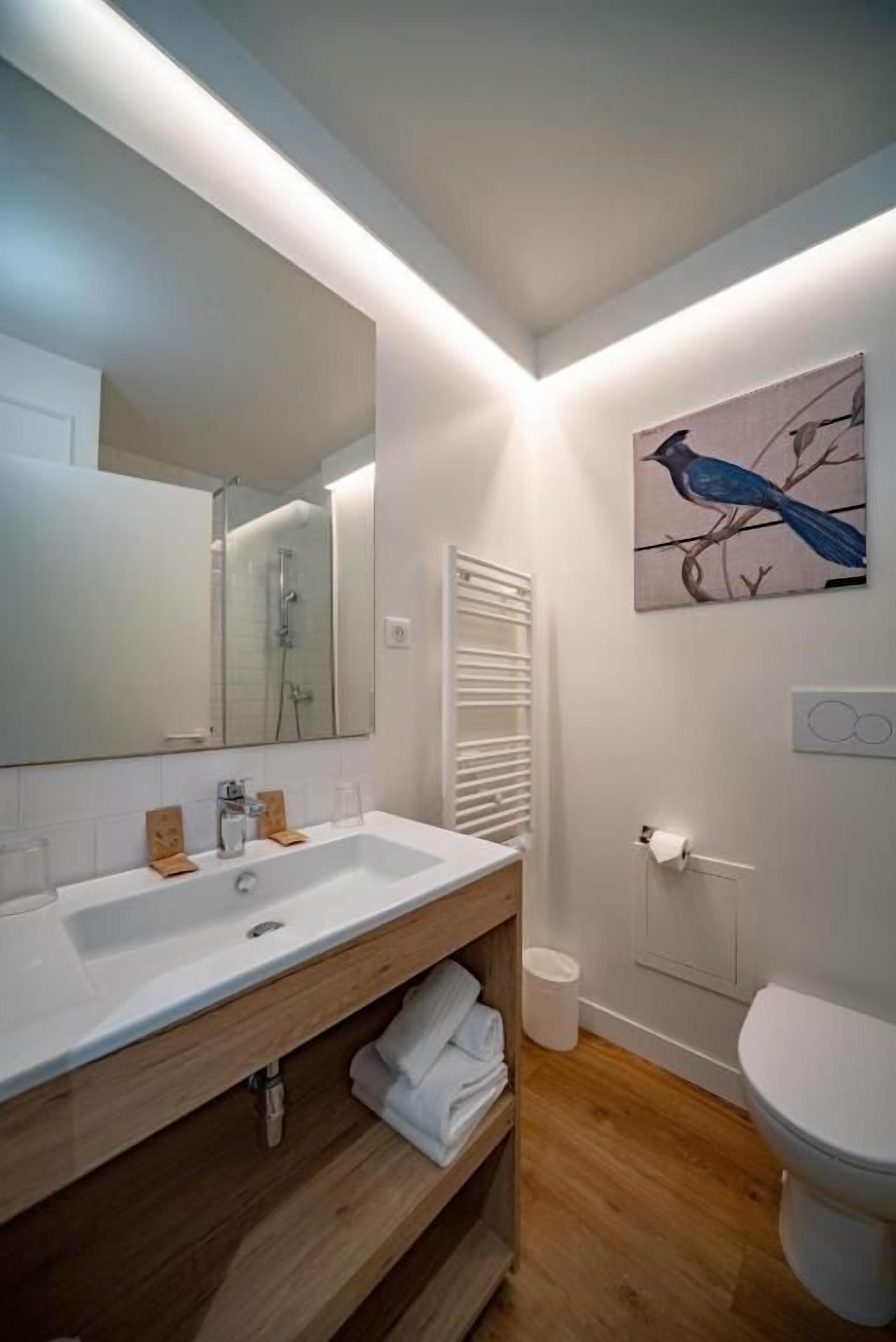 Un baño moderno con un espejo grande, lavamanos blanco, tocador de madera y un inodoro.