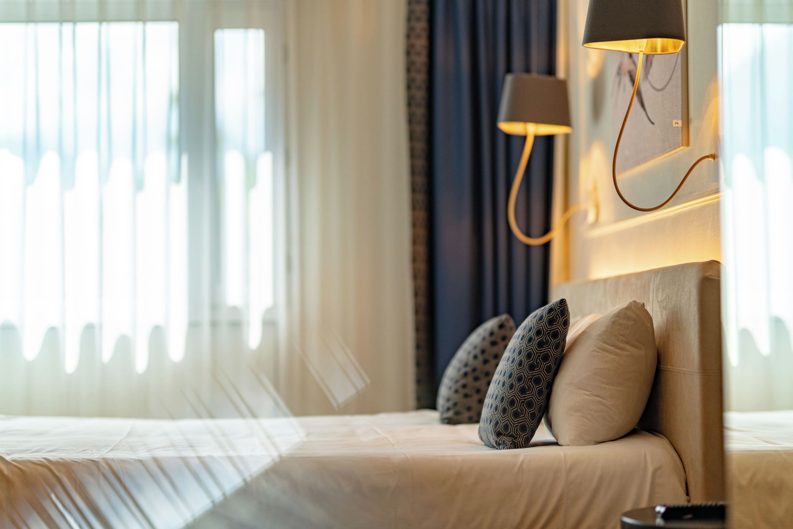 Een hotelkamer met een bed, kussens, een lamp en uitzicht door het raam.