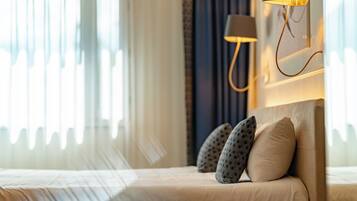 Een hotelkamer met een bed, kussens, een lamp en uitzicht door het raam.