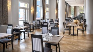 A spacious dining area with multiple tables and chairs, large windows, and modern lighting fixtures.