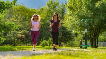 Deux femmes font du jogging sur un sentier dans un parc, avec des arbres et des appareils de musculation en arrière-plan.
