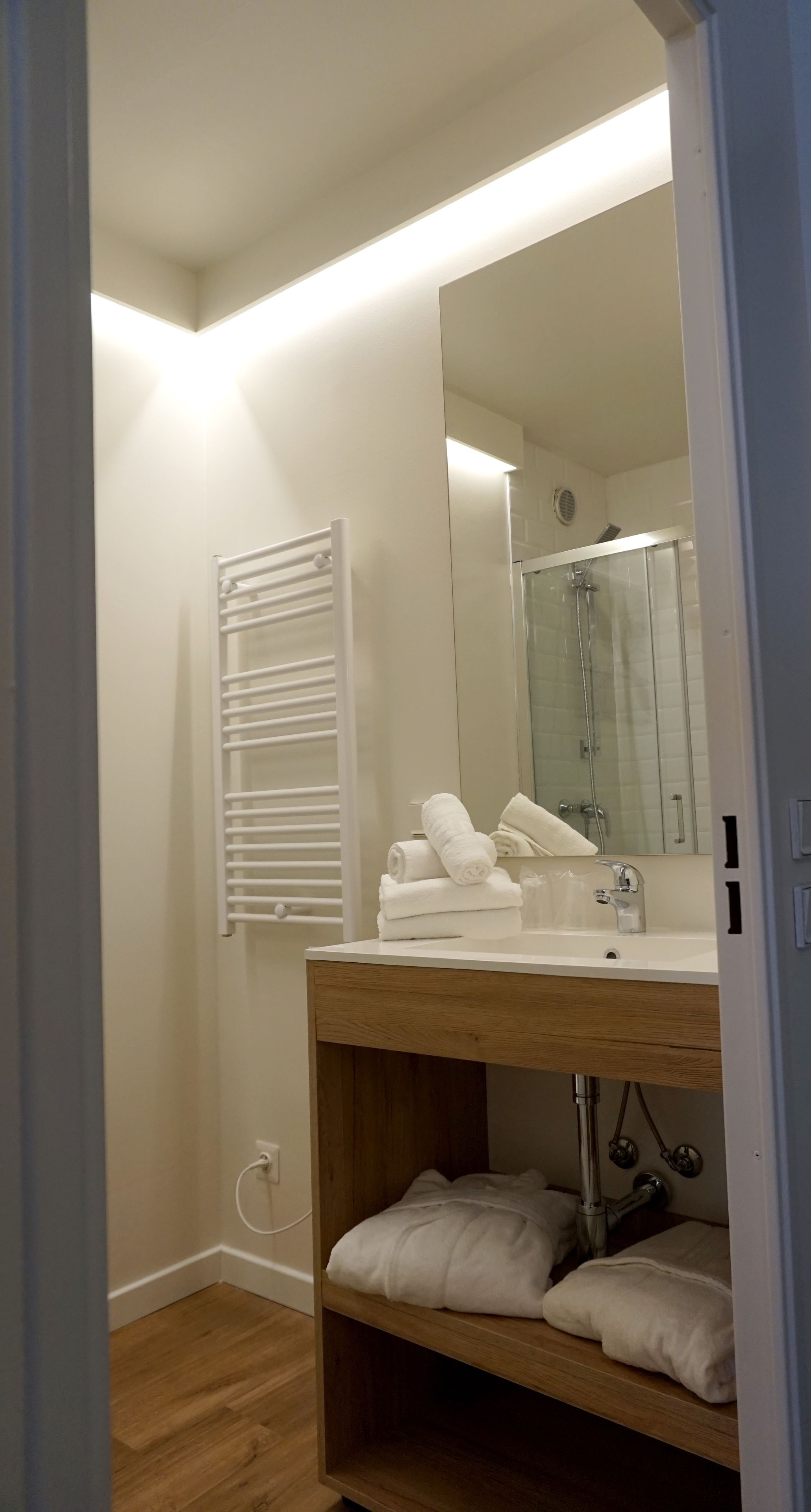 A modern bathroom with a wooden vanity, a large mirror, a glass shower enclosure, and a towel rack.