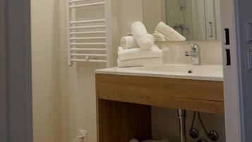 A modern bathroom with a wooden vanity, a large mirror, a glass shower enclosure, and a towel rack.