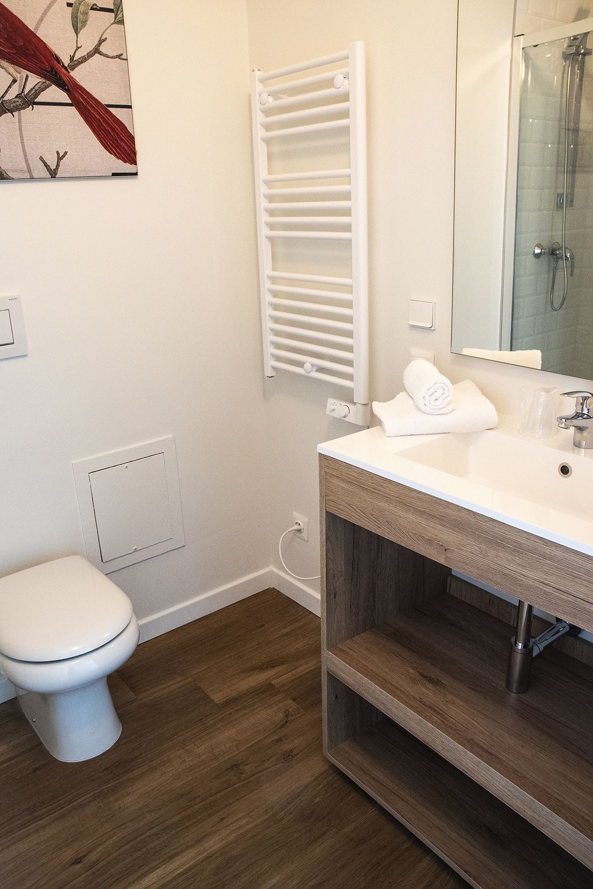 A modern bathroom with a white toilet, a wooden vanity, a white towel, and a glass shower enclosure.