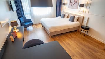 A modern hotel room with a bed, a desk, a chair, a lamp, and a painting on the wall.