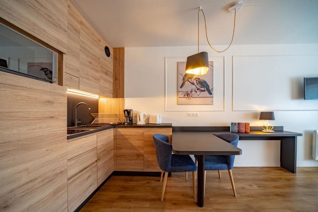 A modern kitchen with wooden cabinetry, a dining area with a table and chairs, and a wall-mounted television.