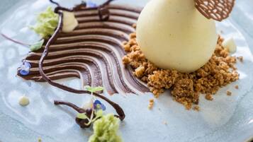 Un dessert su un piatto con glassa al cioccolato, granella e una foglia decorativa.