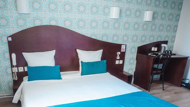 A hotel room with a bed, two pillows, a desk, and a chair. - Hôtel Les Commerçants (Clermont-Ferrand)
