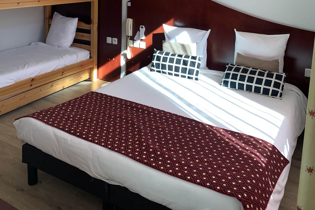 Una habitación de hotel con una cama litera, una cama individual y una manta estampada.