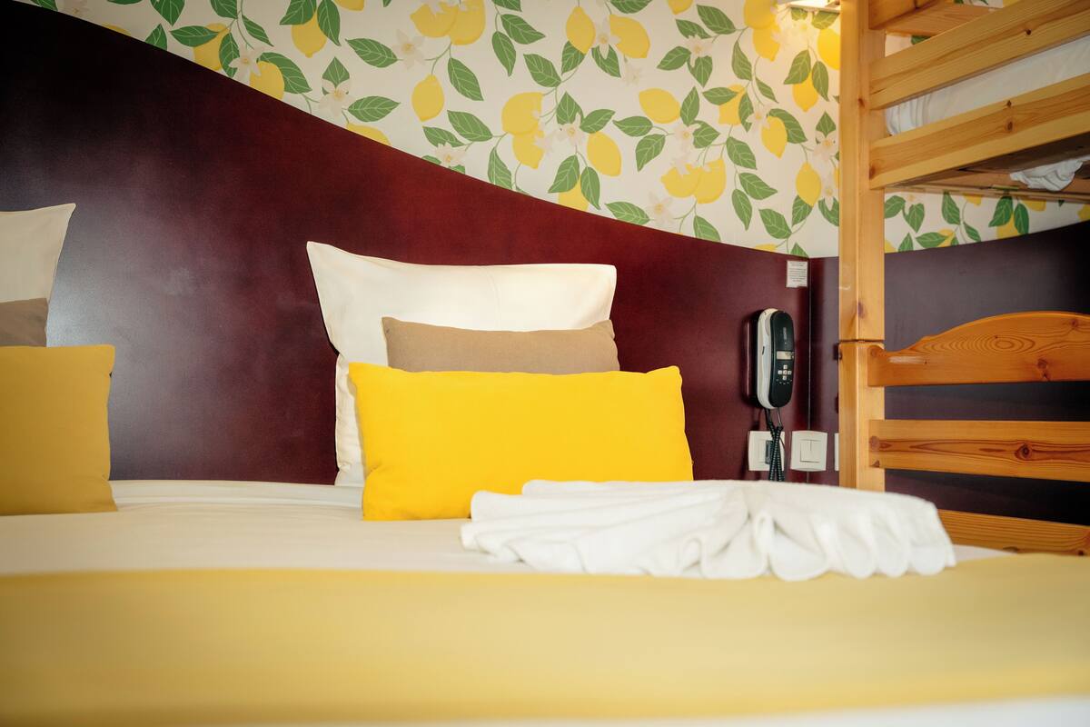 Una habitación de hotel con cama, almohadas, teléfono y literas.