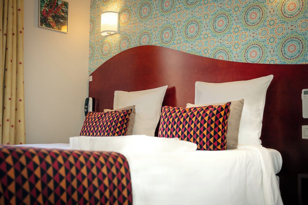 Habitación de hotel con una cama grande, papel tapiz estampado y una lámpara de pared.