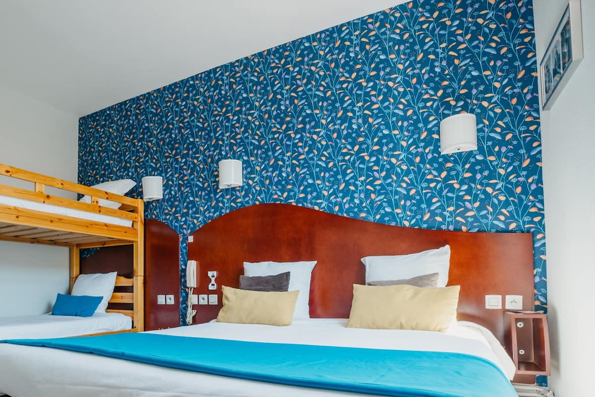 Dormitorio con literas, cabecera de madera, pared con diseño y mesita de noche con lámpara.