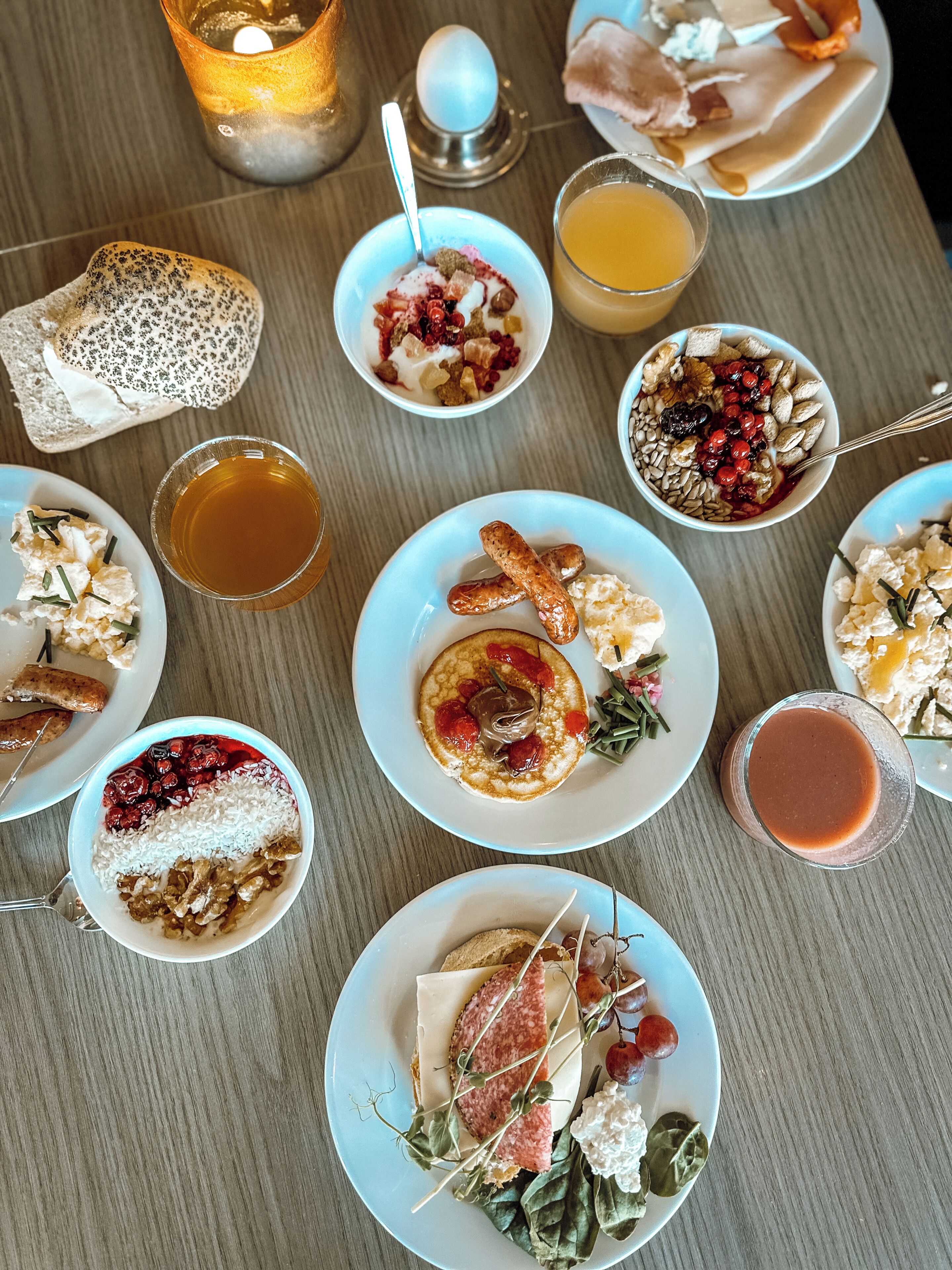 A table with various dishes, including pancakes, sausages, and a plate with cheese and grapes.